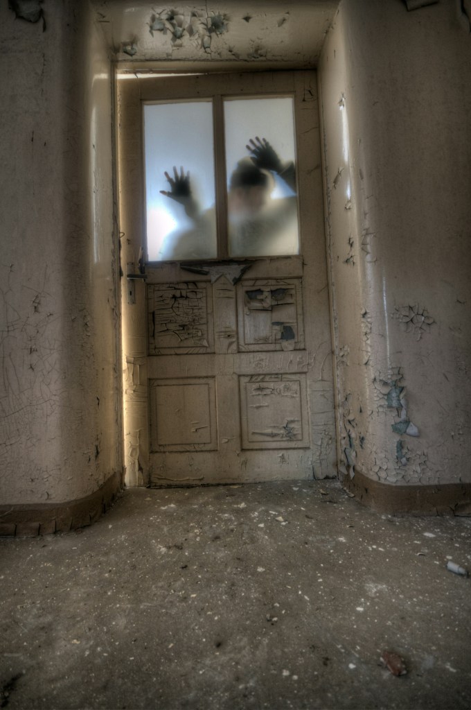 Image: abandoned building with scuffed doorway and chipping paint, a zombie behind the door's glass windows, trying to get to the side where the camera is positioned