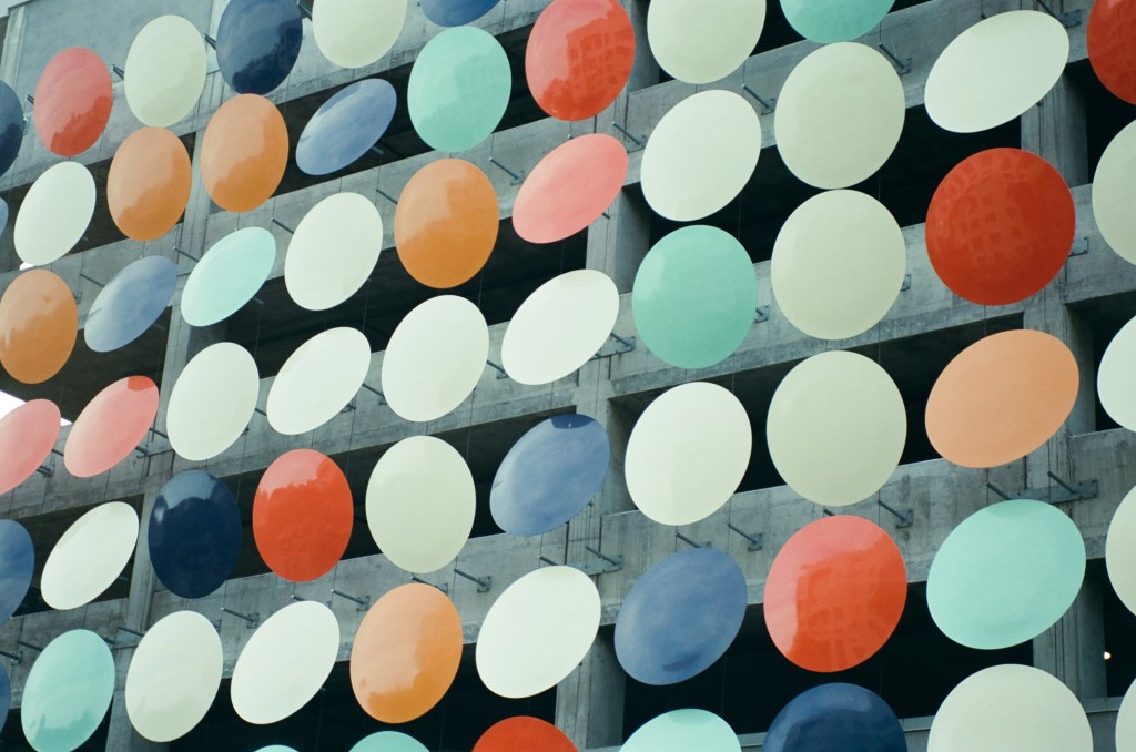 Image: multicolored, reflective, circular cut-outs protruding from the side of a parking garage